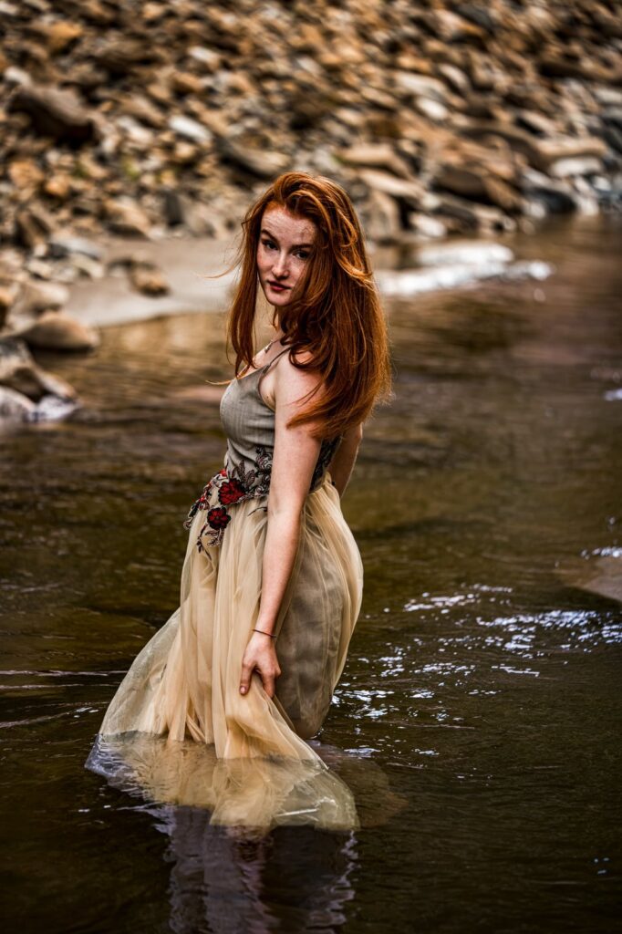 Model im Kleid mit Tüllrock steht im Fluss und blickt über die Schulter zurück