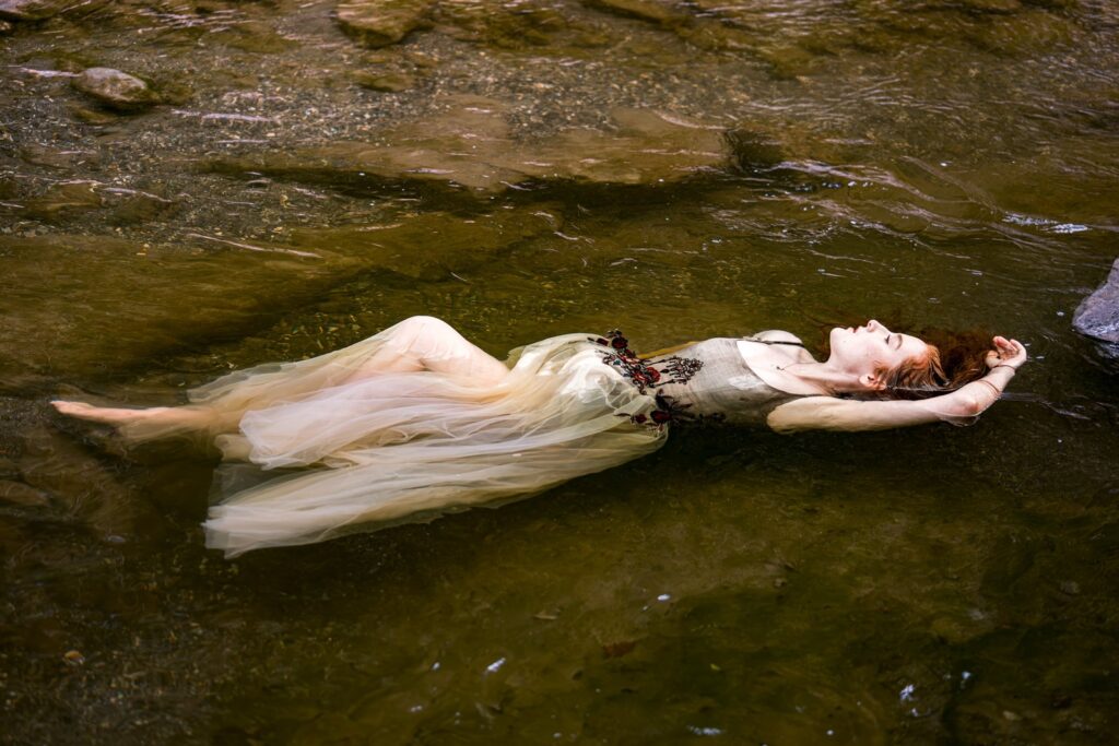Model treibt im Kleid auf dem Wasser, der nudefarbene Tüllrock breitet sich auf der Oberfläche aus