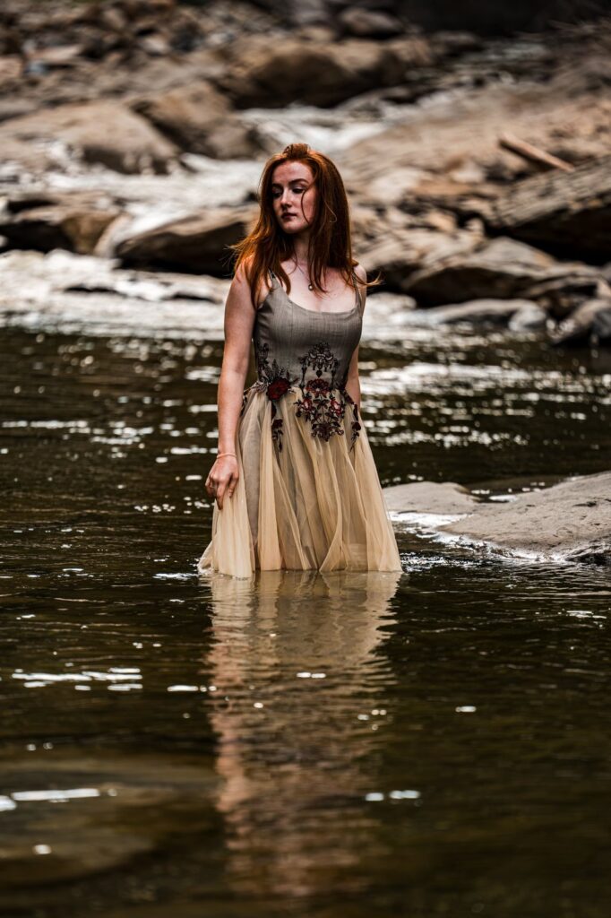 Model steht im handbestickten Kleid knietief im Fluss