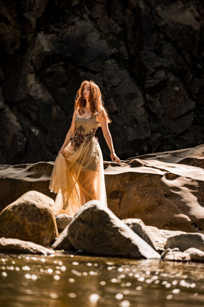Model im Kleid auf den Felsen am Fluss, Tüllrock im Gegenlicht