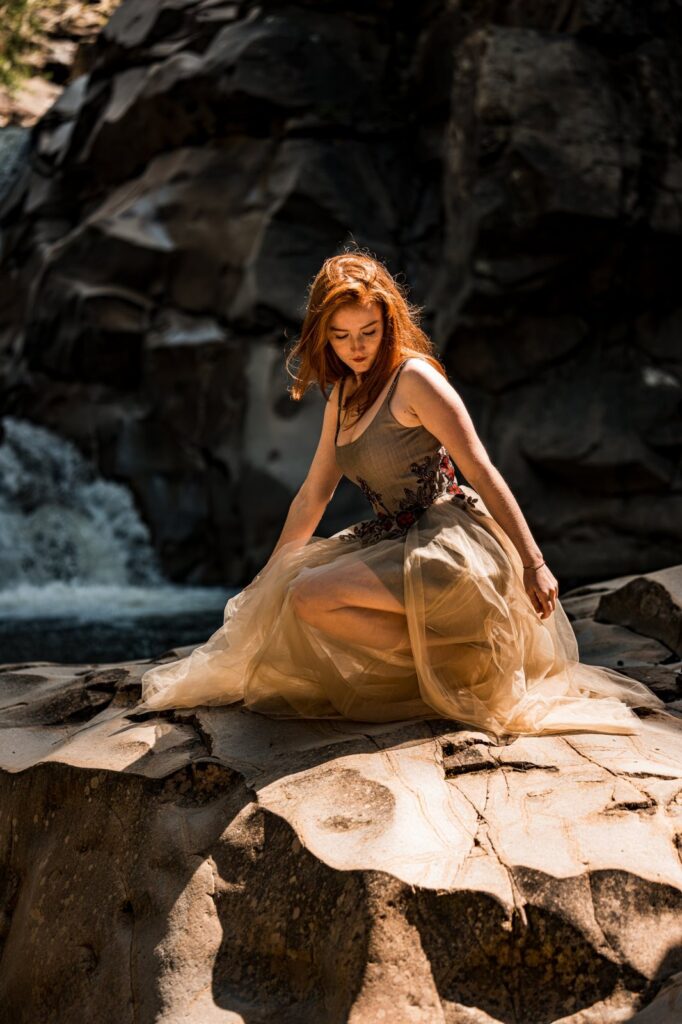 Model kniet im Kleid auf dem Felsen und blickt nach unten