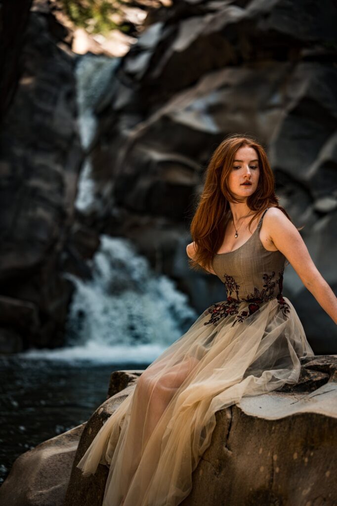 Model sitzt im Kleid vor dem Wasserfall, Nahaufnahme von Korsage und Stickerei