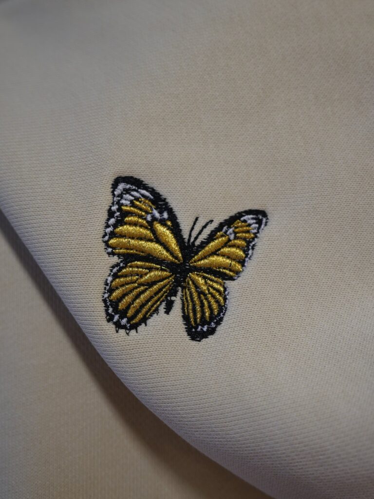 Gestickter Schmetterling aus goldenen Metallfäden auf cremefarbenem Hoodie