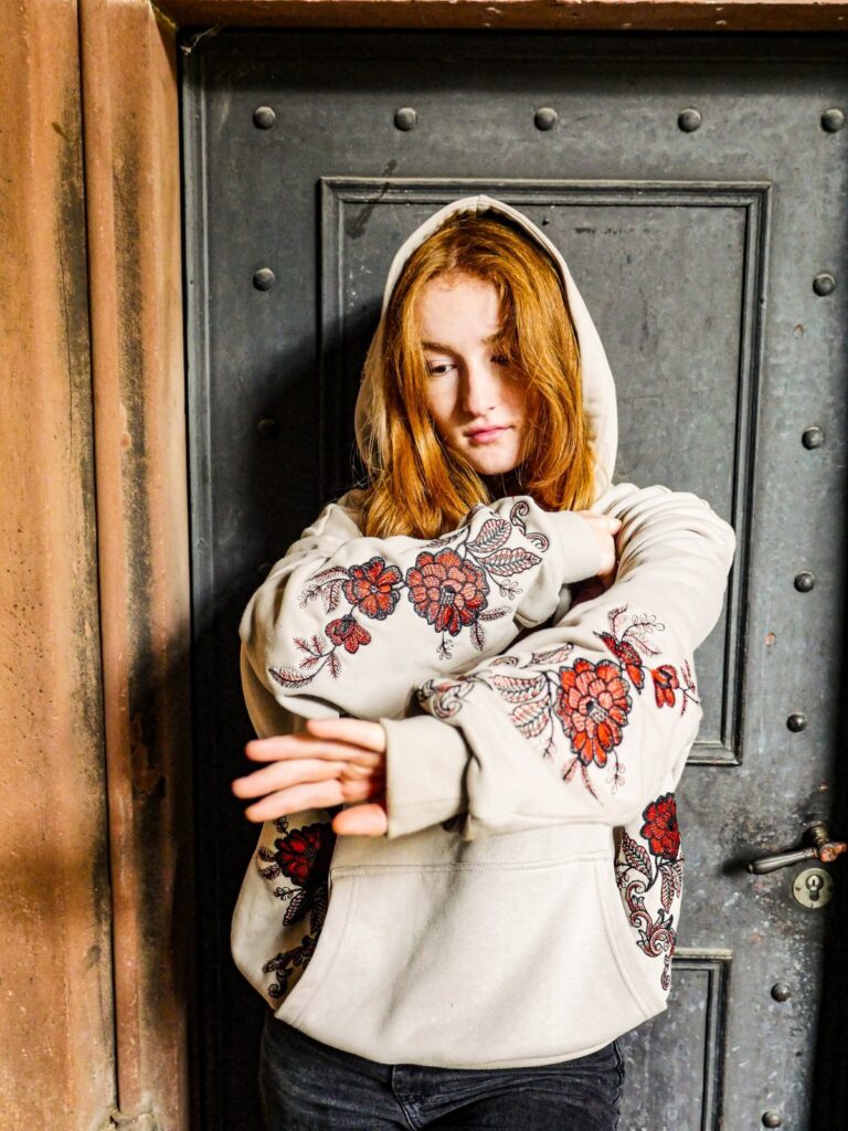 Model mit Kapuze verschränkt die Arme, rote und schwarze Blumenranken auf den Ärmeln des Oversize Hoodies